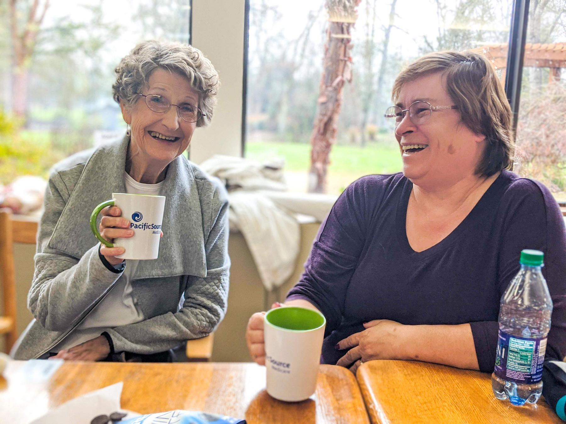 Two older adults drink coffee while laughing at Willamalane Adult Activity Center