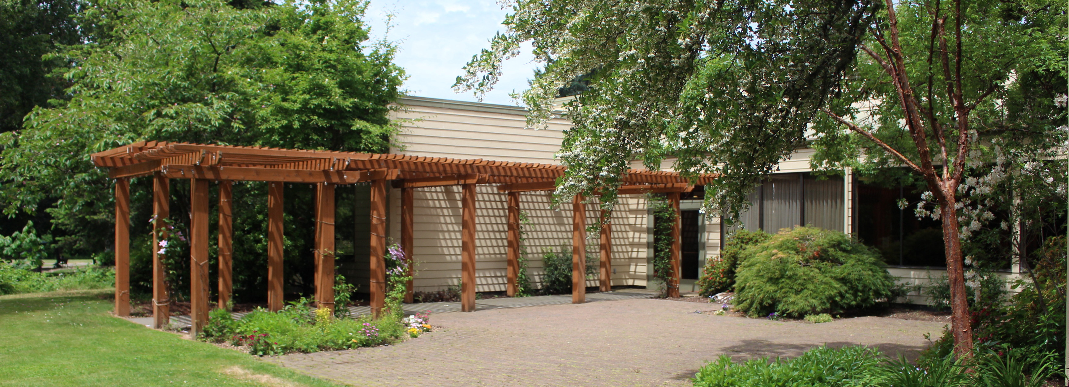 An outdoor patio with a wooden pergola and blooming trees with vast open space available for events