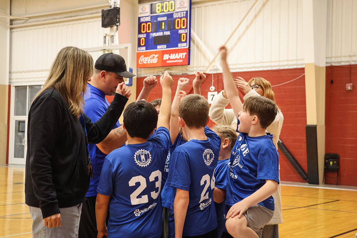 Kids team of basketball players huddle and cheer with their coach