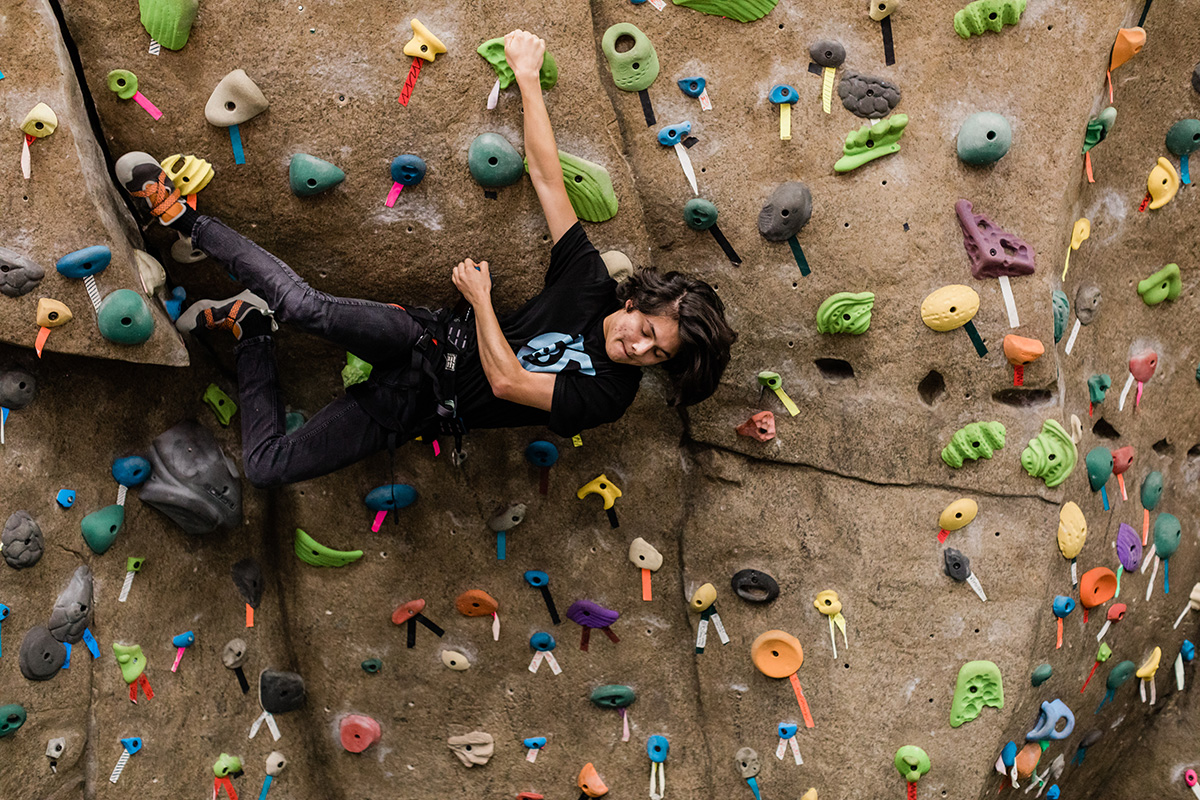 Young man hanging sideways climbs a rock wall