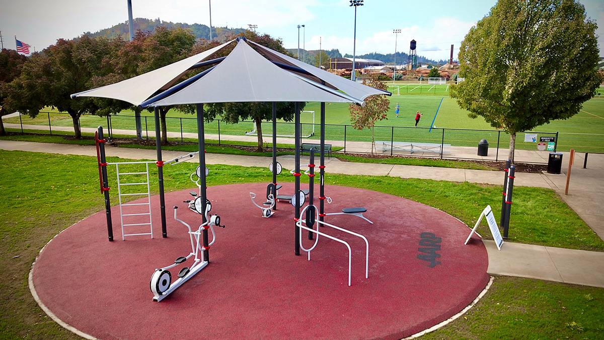 An outdoor, shaded area with fitness equipment near sports fields