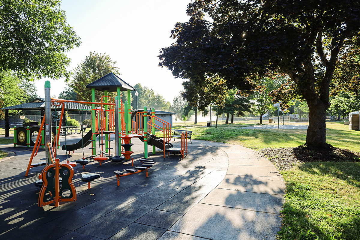 A colorful playground with the sun peaking through the trees at Meadow Park