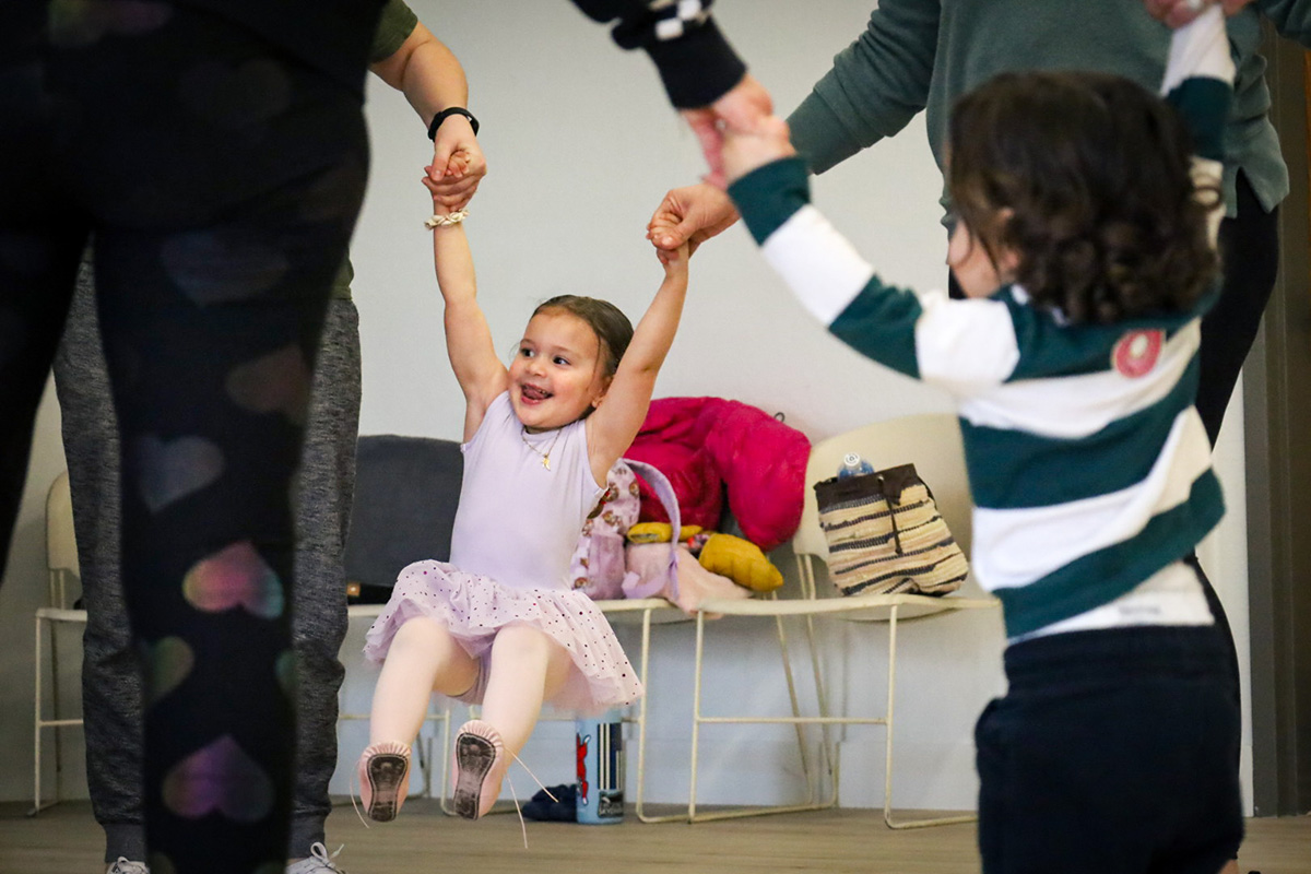 Smiling toddlers hold adults hands in a circle during a class