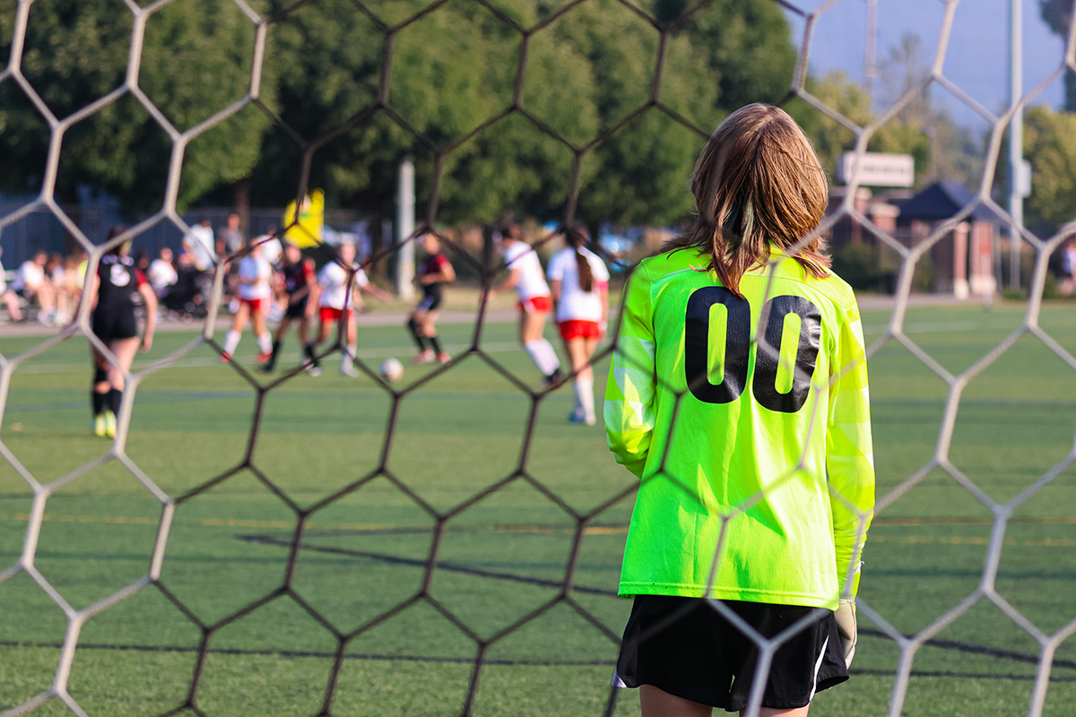 A goalie stands in a soccer net watching other players approaching her net