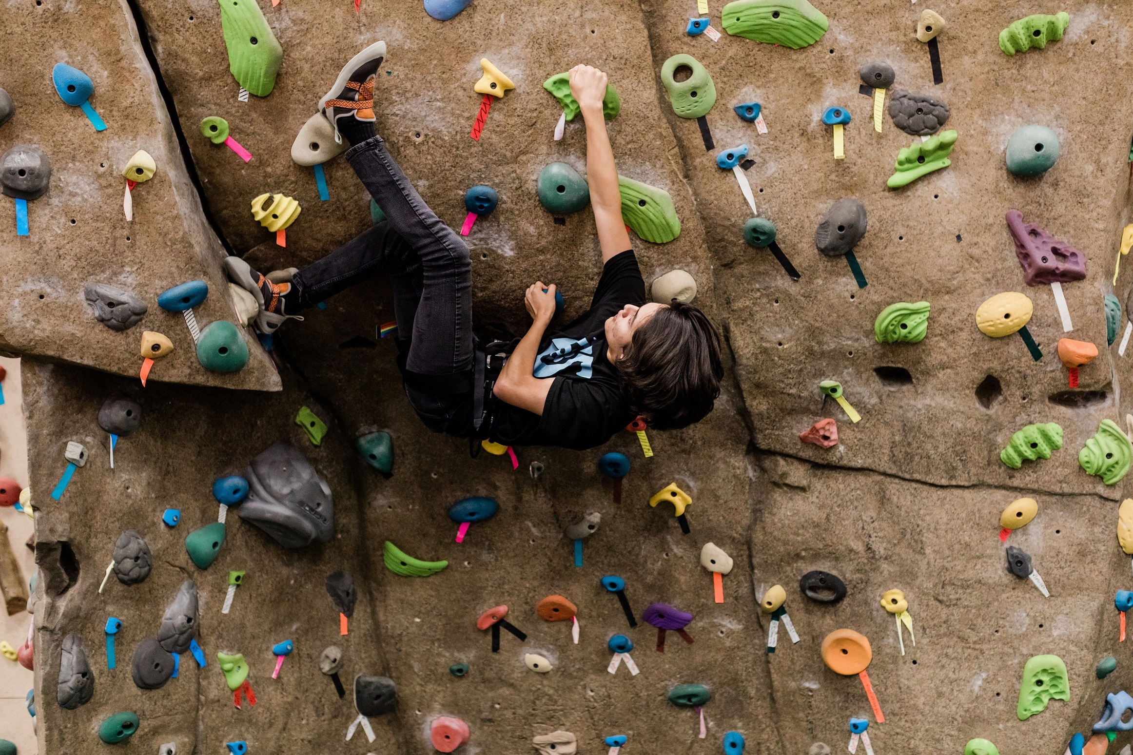 Adult man with dark hair scaling a rock climbing wall.
