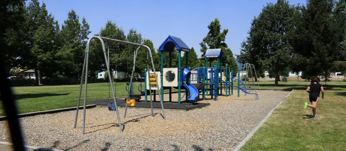 Pride Park Playground. Slide, swings, playground equipment, and a running child. 