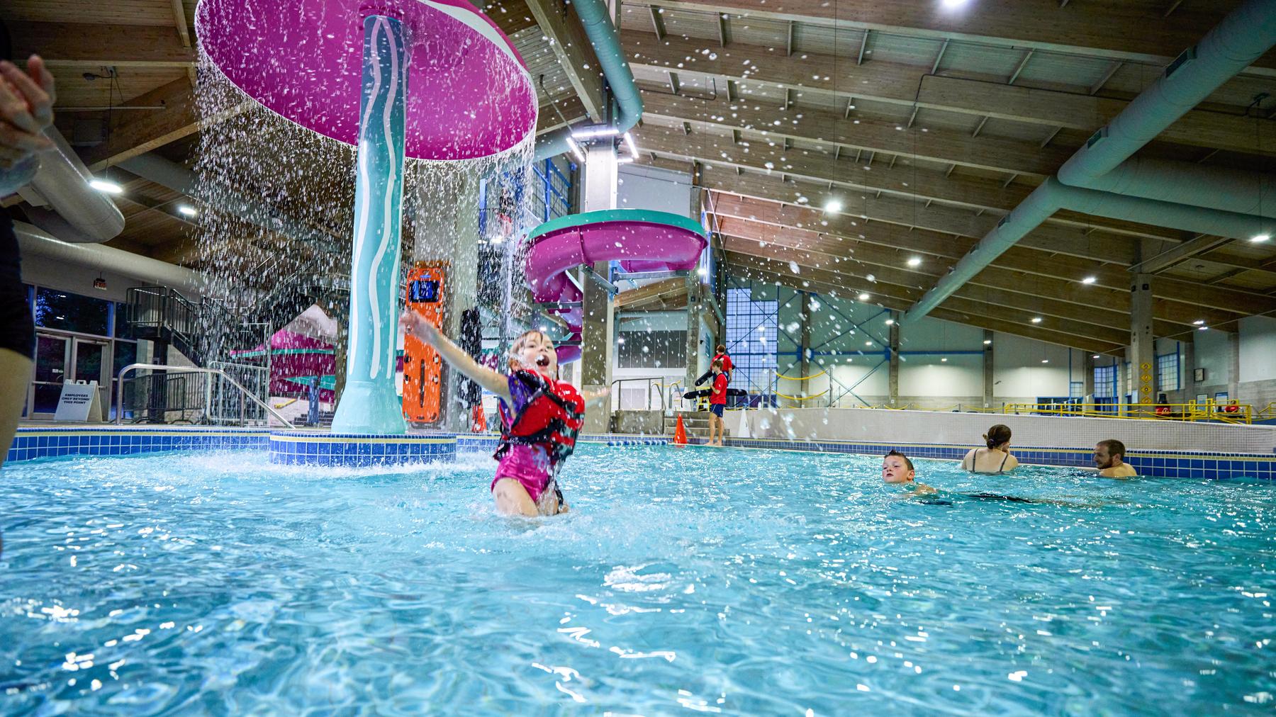 Young child wearing lifejacket plays near jellyfish water fountain at the pool