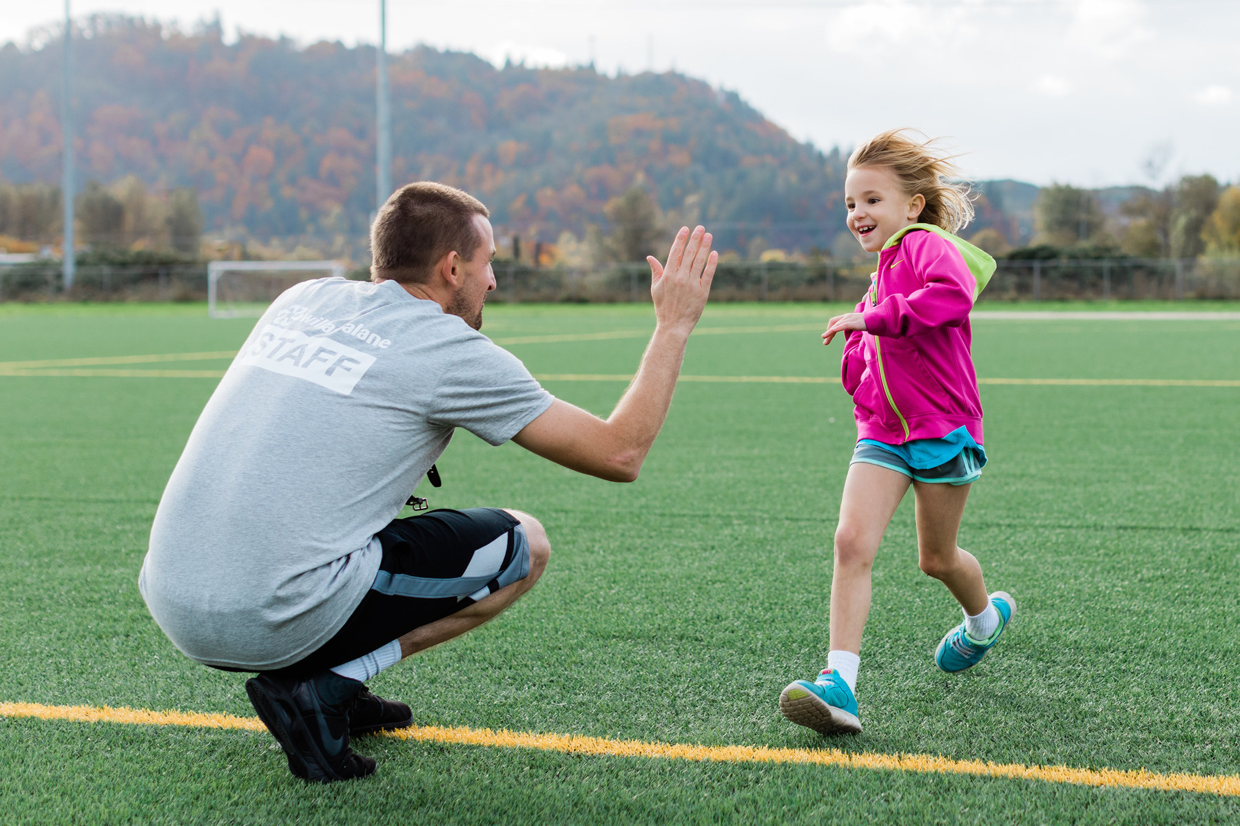 Willamalane staff member high fives young child running on turf field