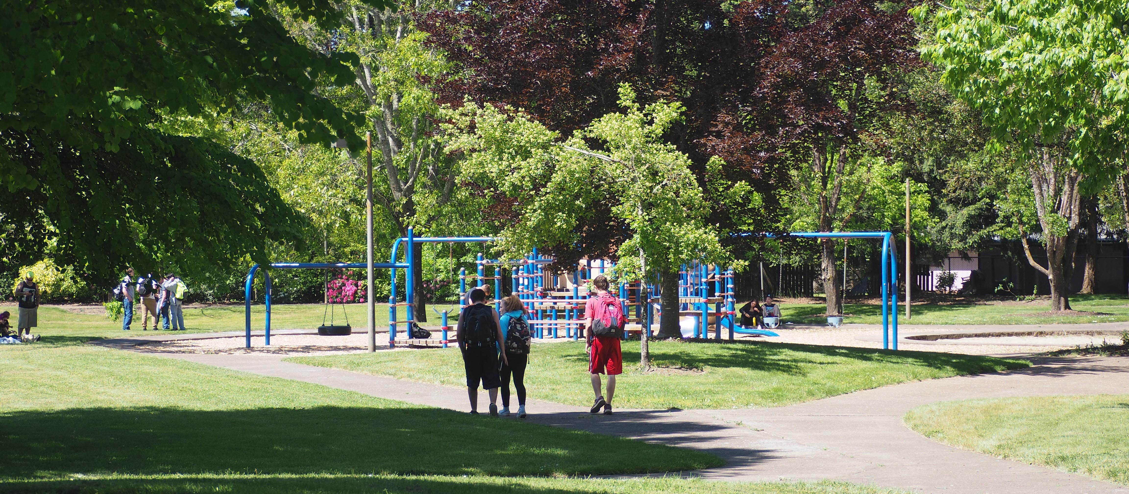 Students walking with backpacks on a paved path toward a playground