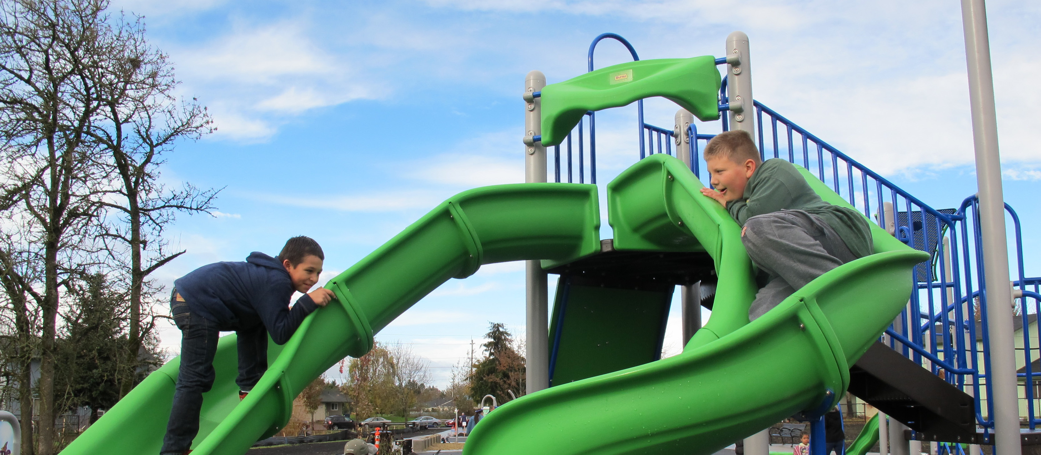 Two kids slide down two curved slides at Pacific Park