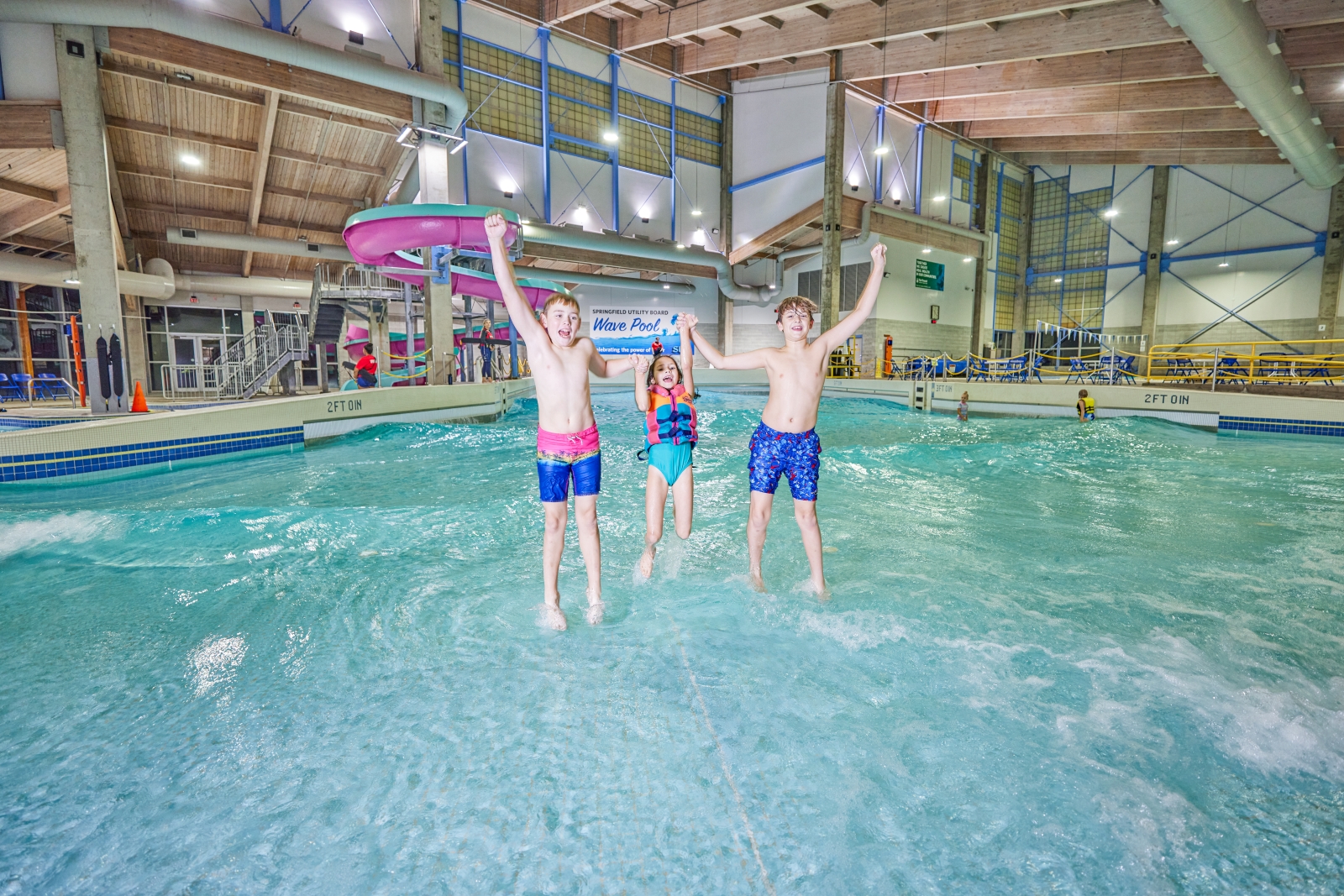 Three kids jumping in the water at an indoor pool.