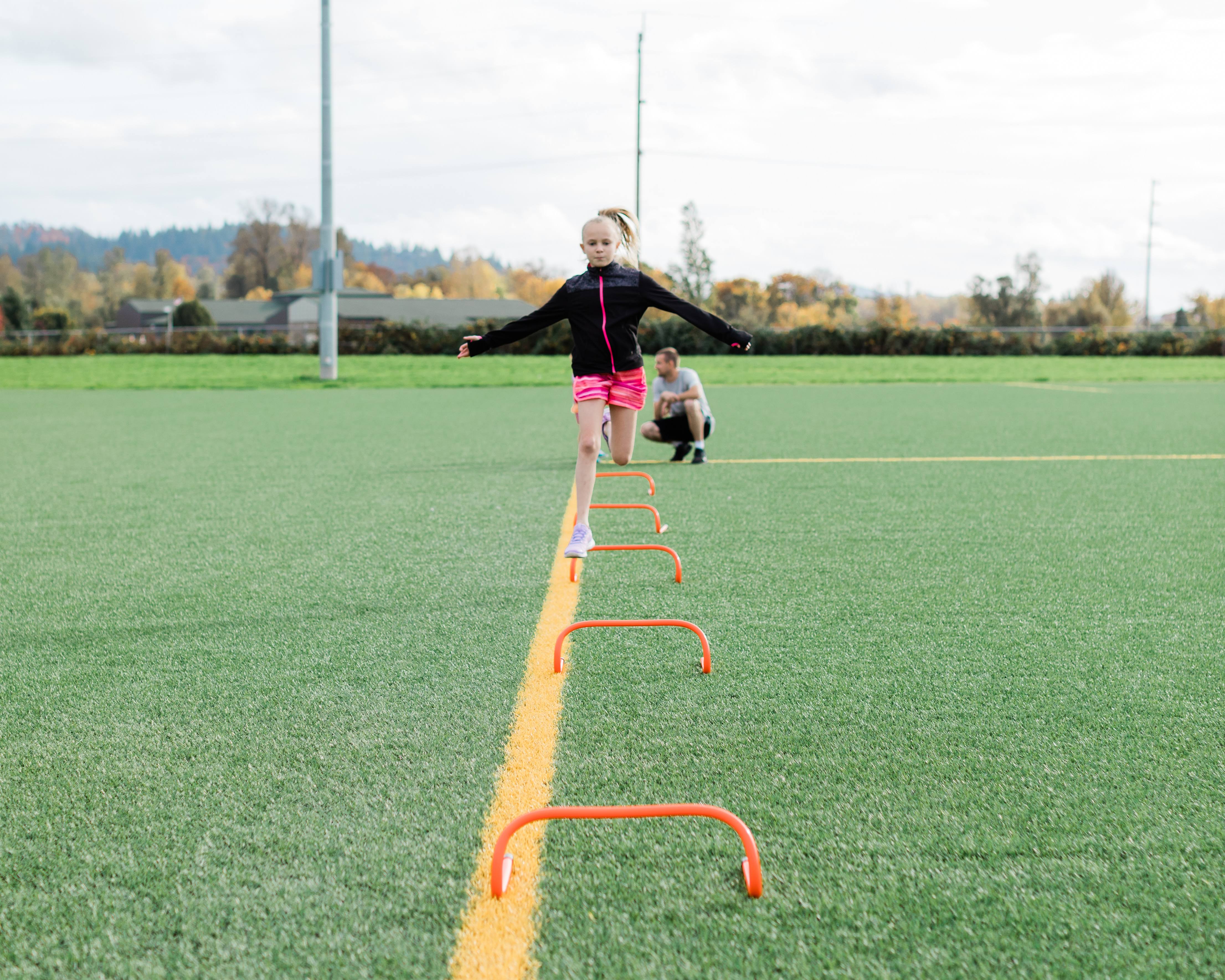Track and field athlete training on a field and jumping over a small hurdle.
