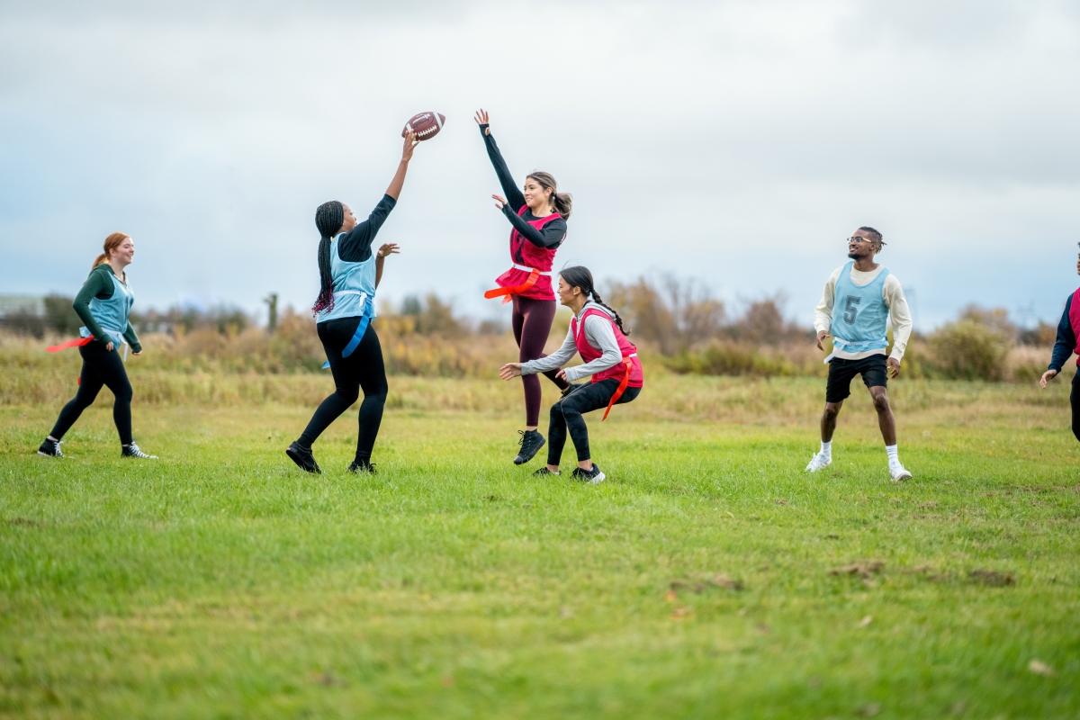 Two teams tossing a football on a green grass field.