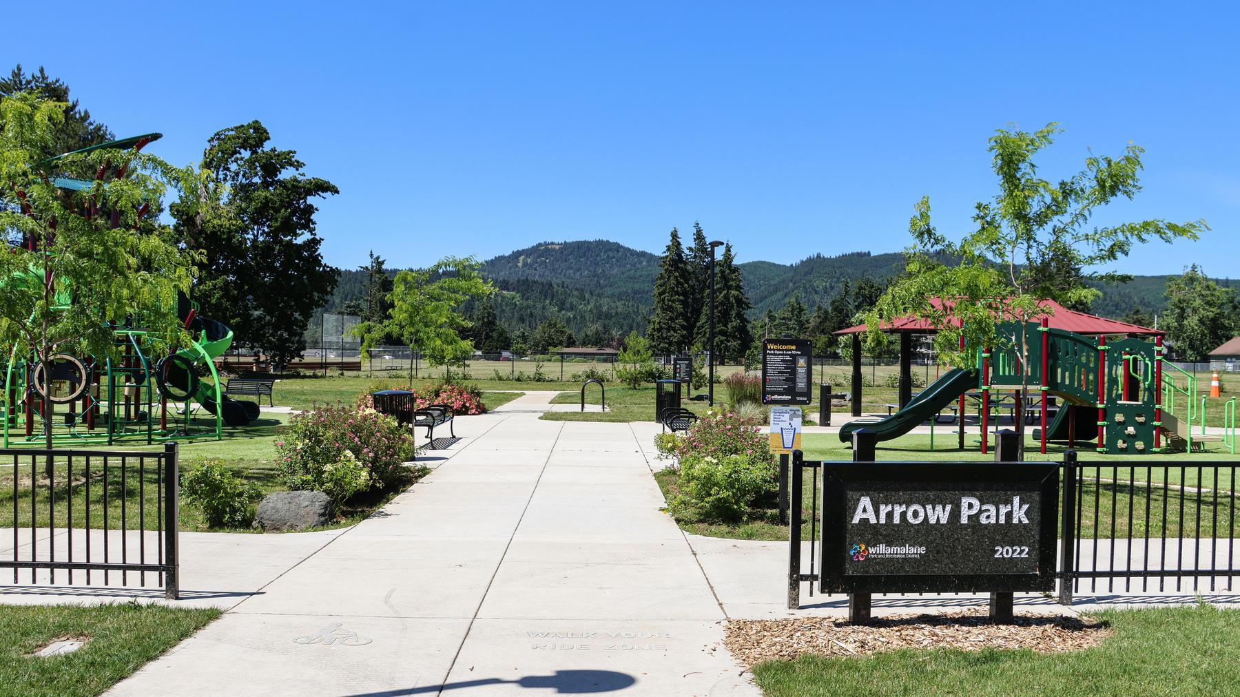 View of Arrow Park entry featuring park sign, paved paths, and two playground structures