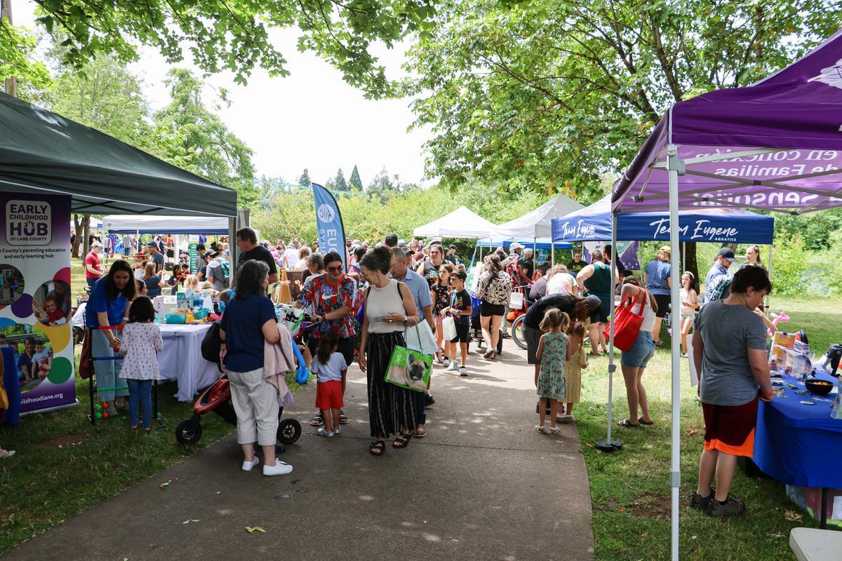 A crowd of people walk on a paved path between two rows of outdoor tents with activities.