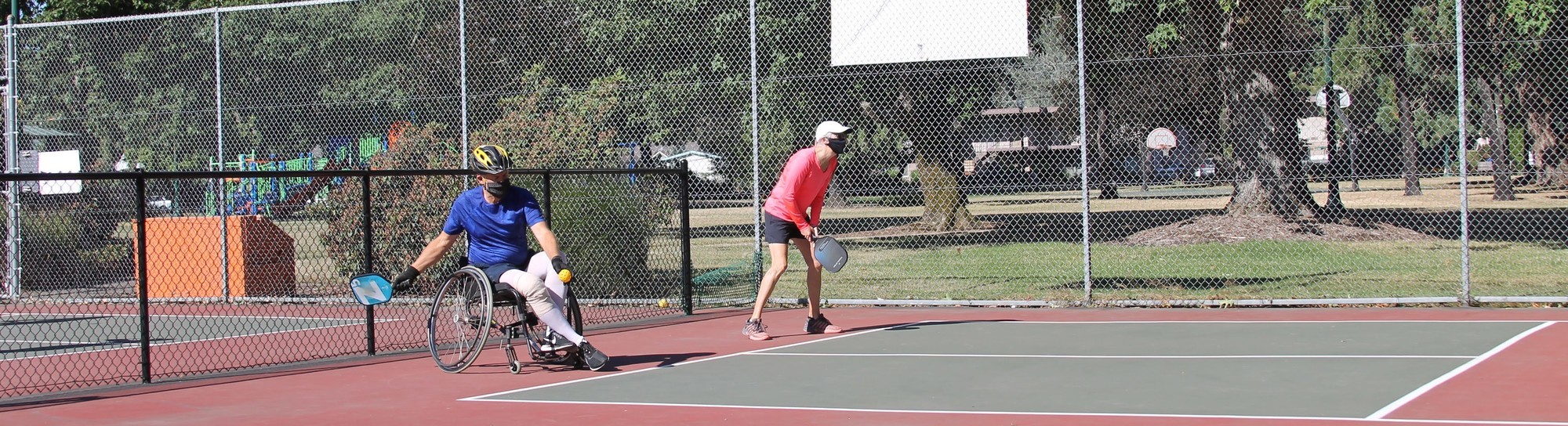 A person standing and another using a wheelchair plays pickleball