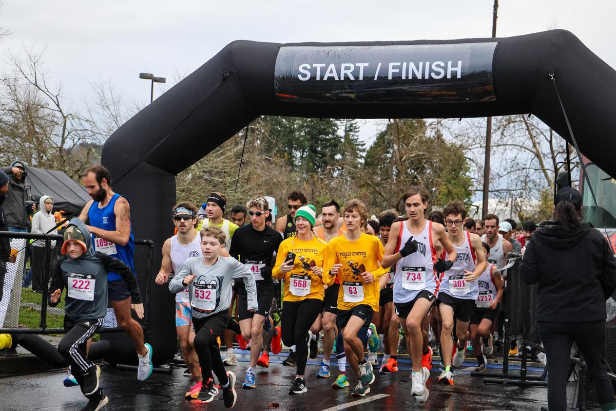 A large group of runners takes their first steps across the starting line on race day.