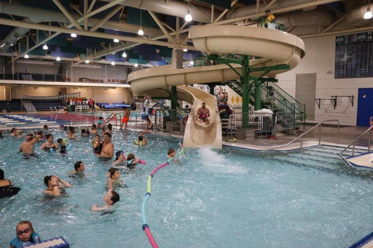 People swimming in an indoor pool, adult and child go down waterslide together