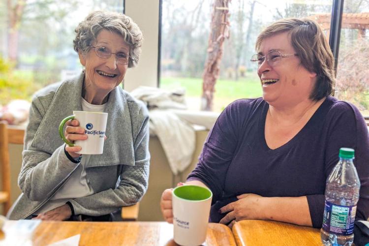 Two older adults drink coffee while laughing at Willamalane Adult Activity Center