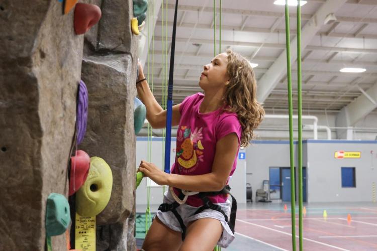 A young climber plots their next hold, while dangling from a top rope on a rock wall.