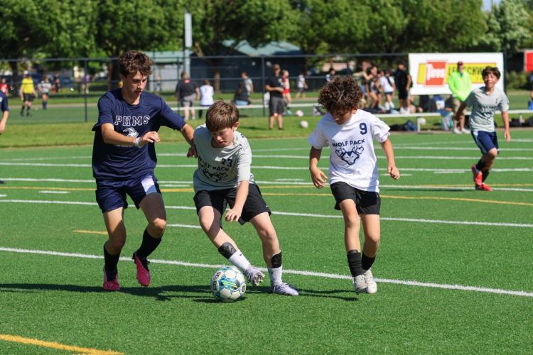 Three players compete for a soccer ball on an outdoor field.