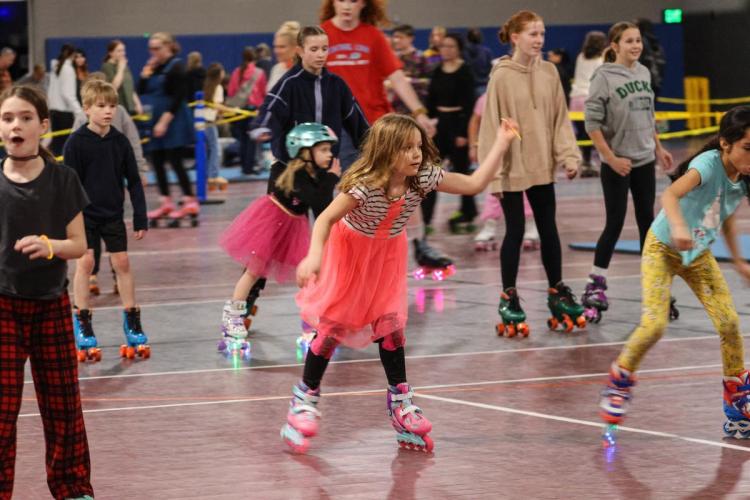 A child in a pink skirt balances on rollerblades.