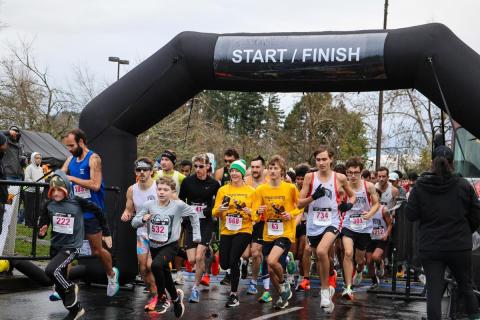 A large group of runners takes their first steps across the starting line on race day.