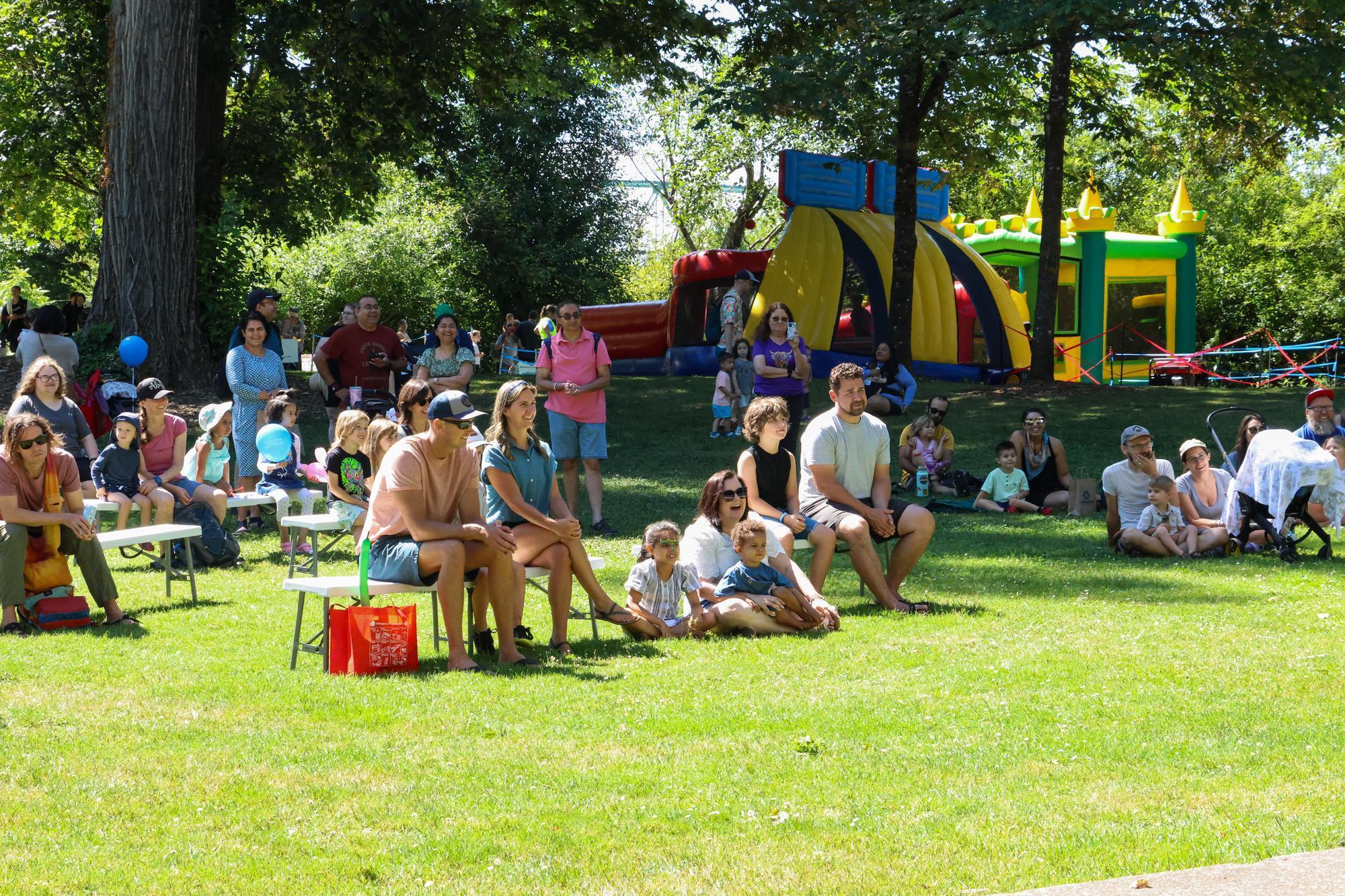 A group of people sit on the grass watching a performance.