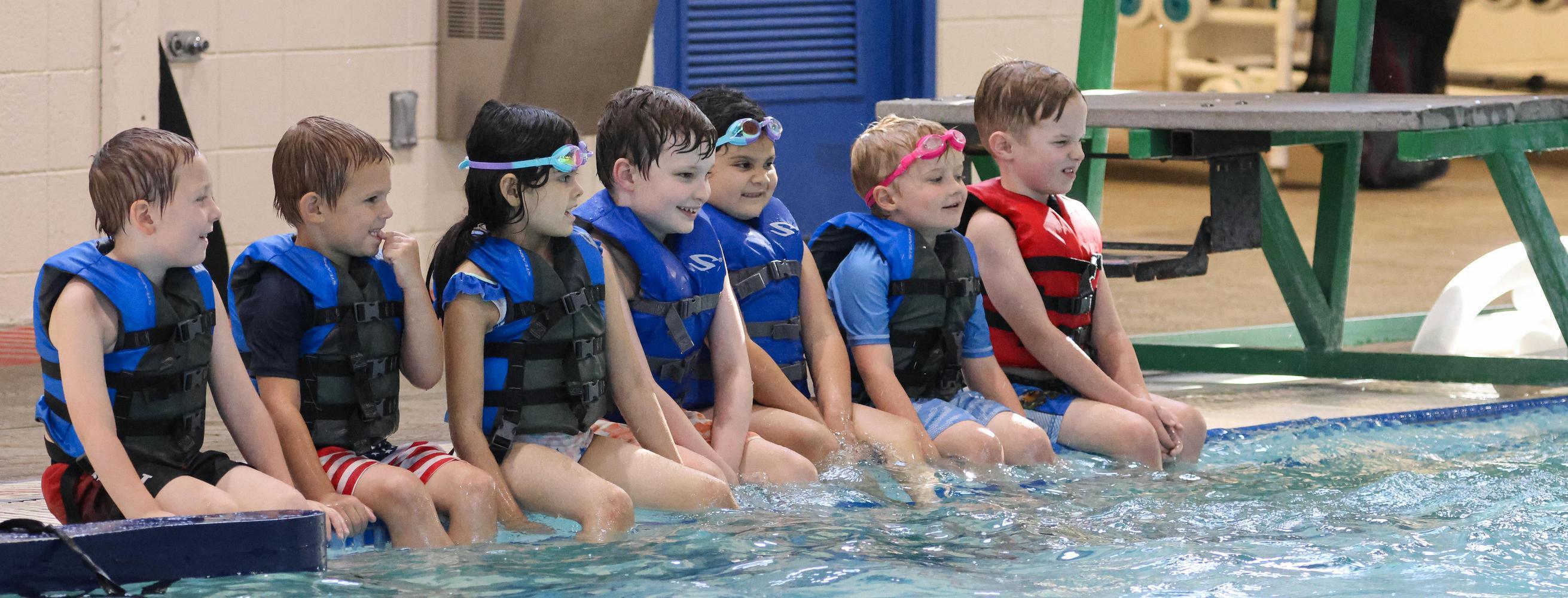 Kids sit on side of pool during swim lessons