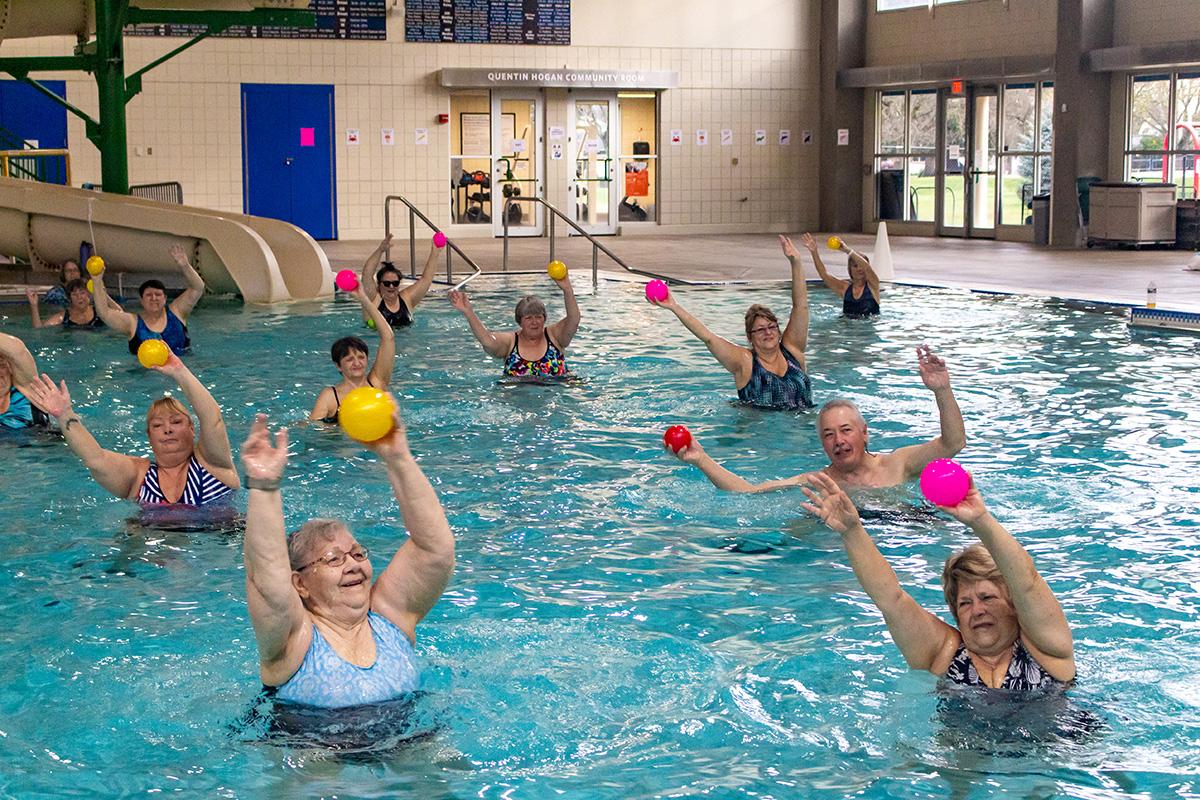 Community members in a pool hold soft balls above their heads during a water fitness class