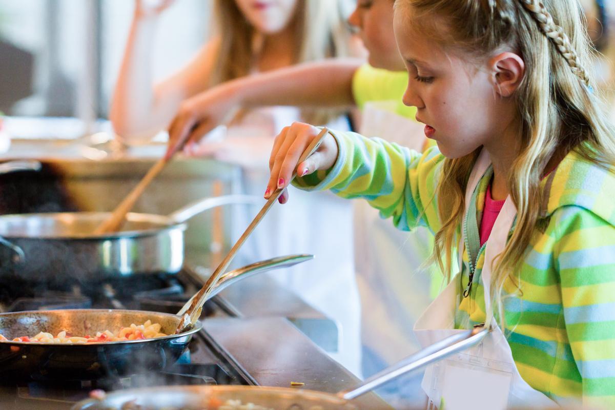 A child stirs a pot of pasta in an instructional cooking class.
