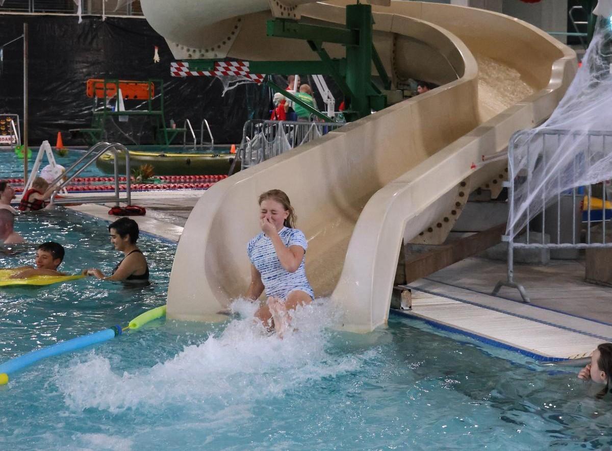 A teenager floats down a waterslide, splashing into the pool below.