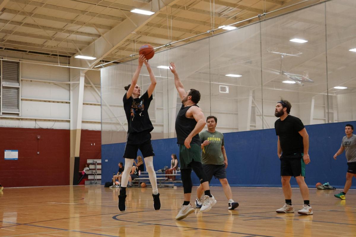 Adults play basketball in an indoor gym.