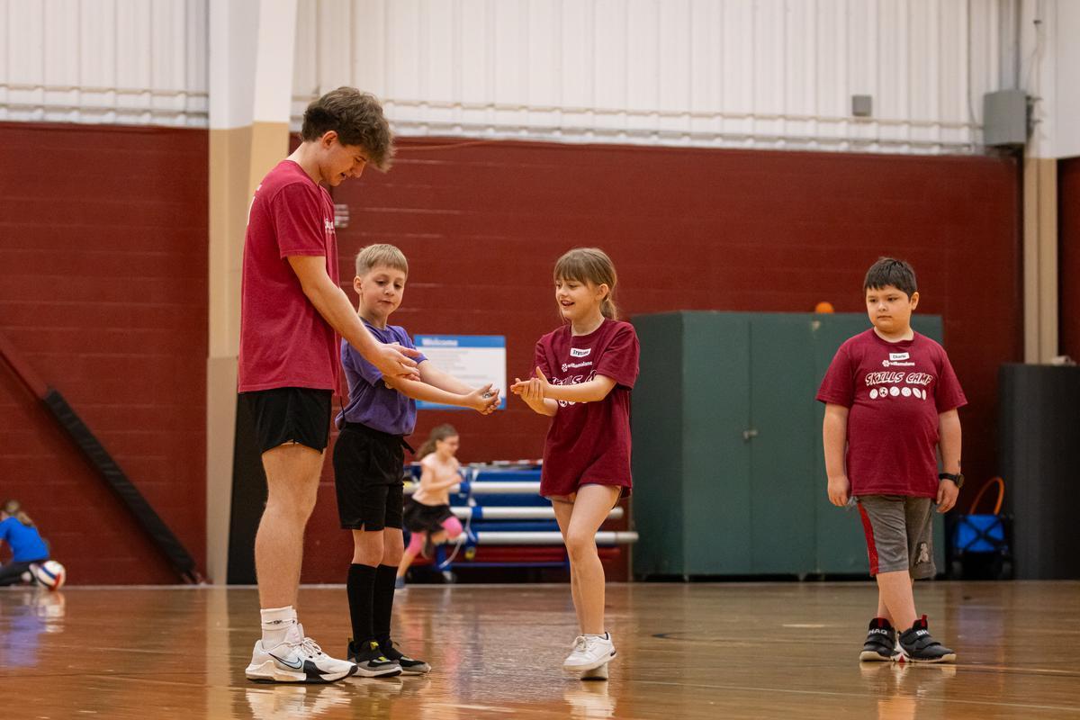 An adult demonstrates proper sports movements to three kids.