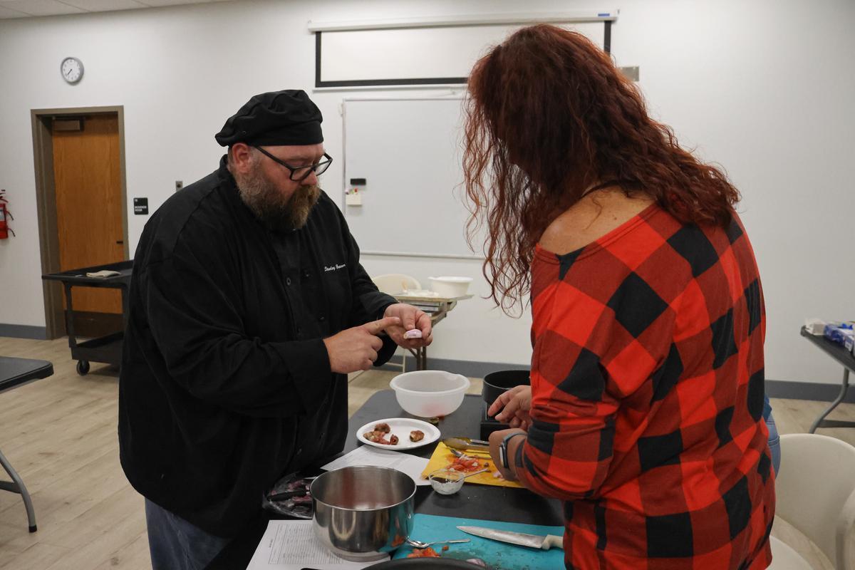 Two adults stand and point to food in their hands.