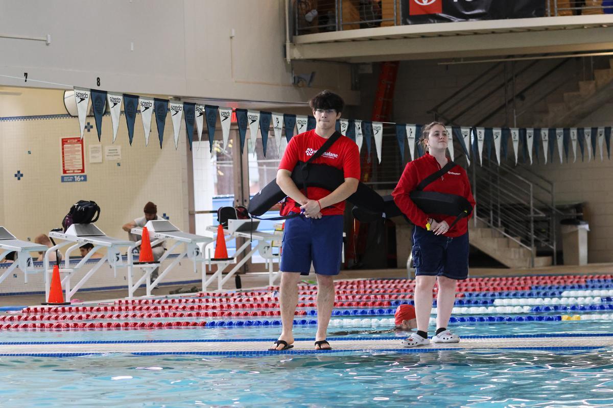 Two adults in red shirts stand watch next to a pool.