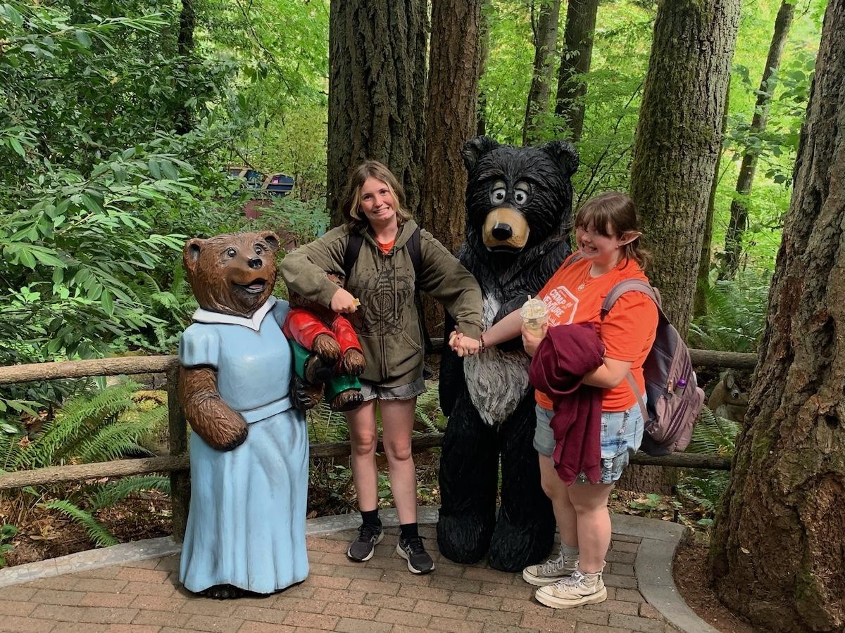 Two teens stand next to life-sized animals at a theme park.
