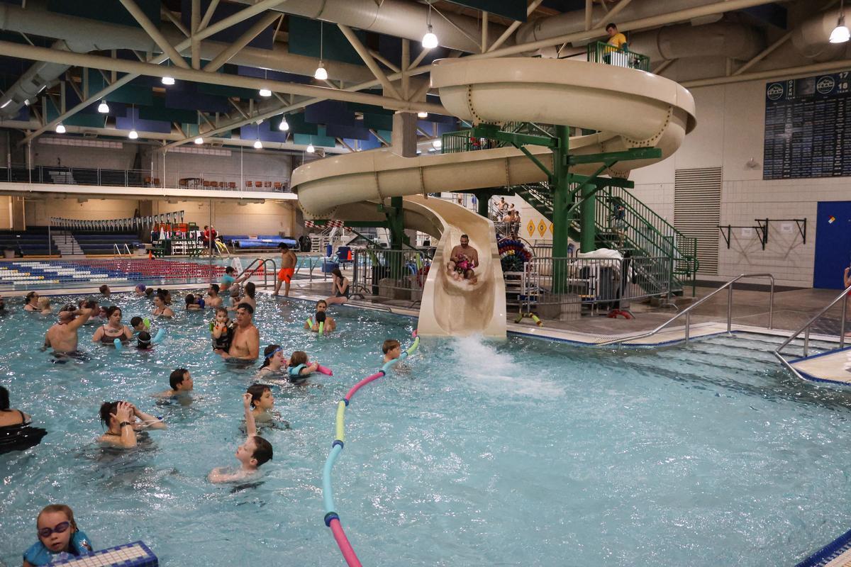People swimming in an indoor pool, adult and child go down waterslide together