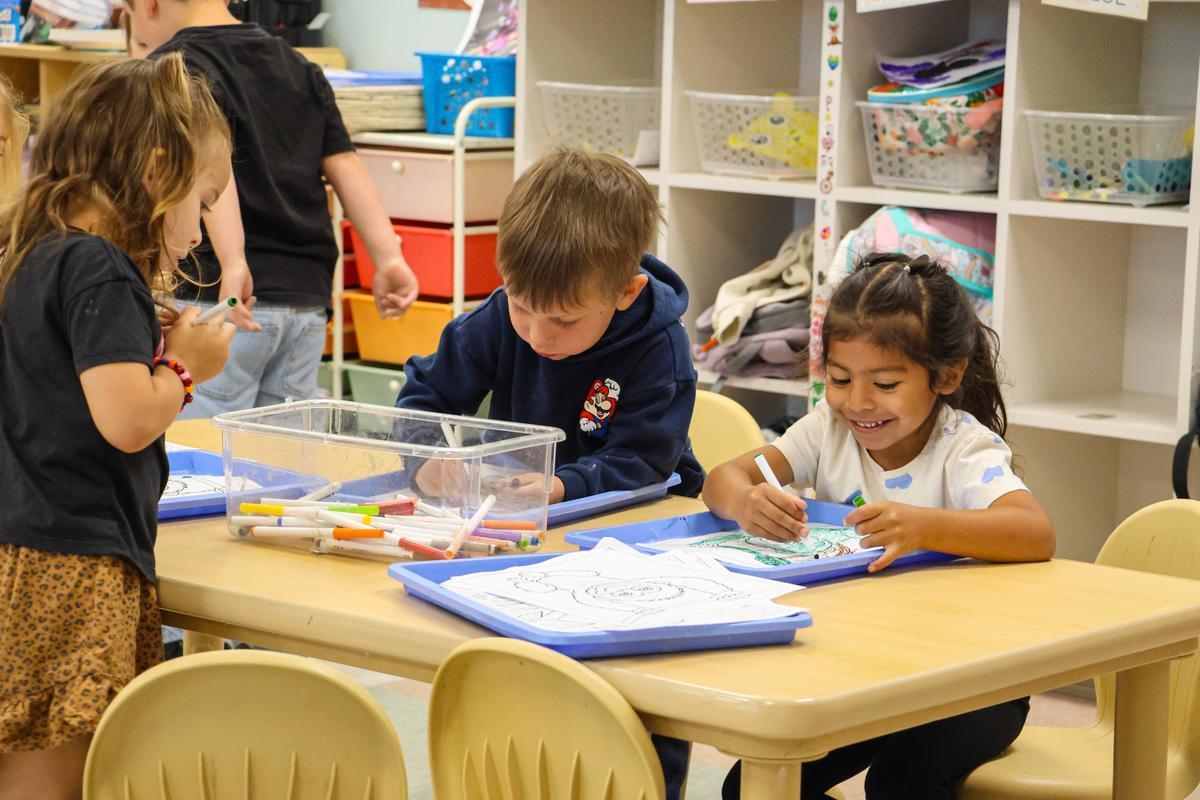 Three children sit around a table drawing.