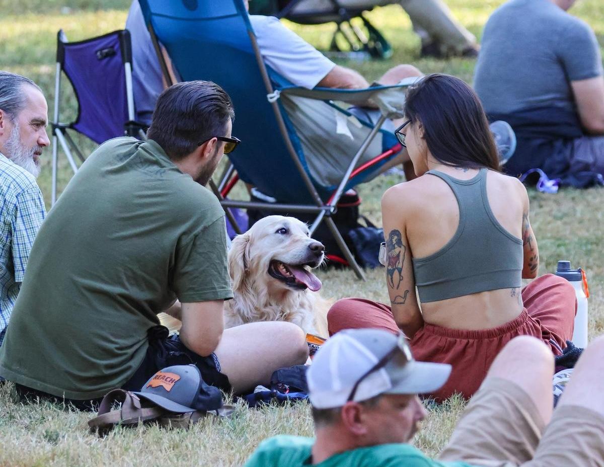 A group of people sit with a dog on the grass.
