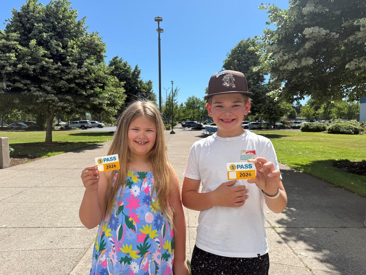 Two kids stand holding their 1pass cards