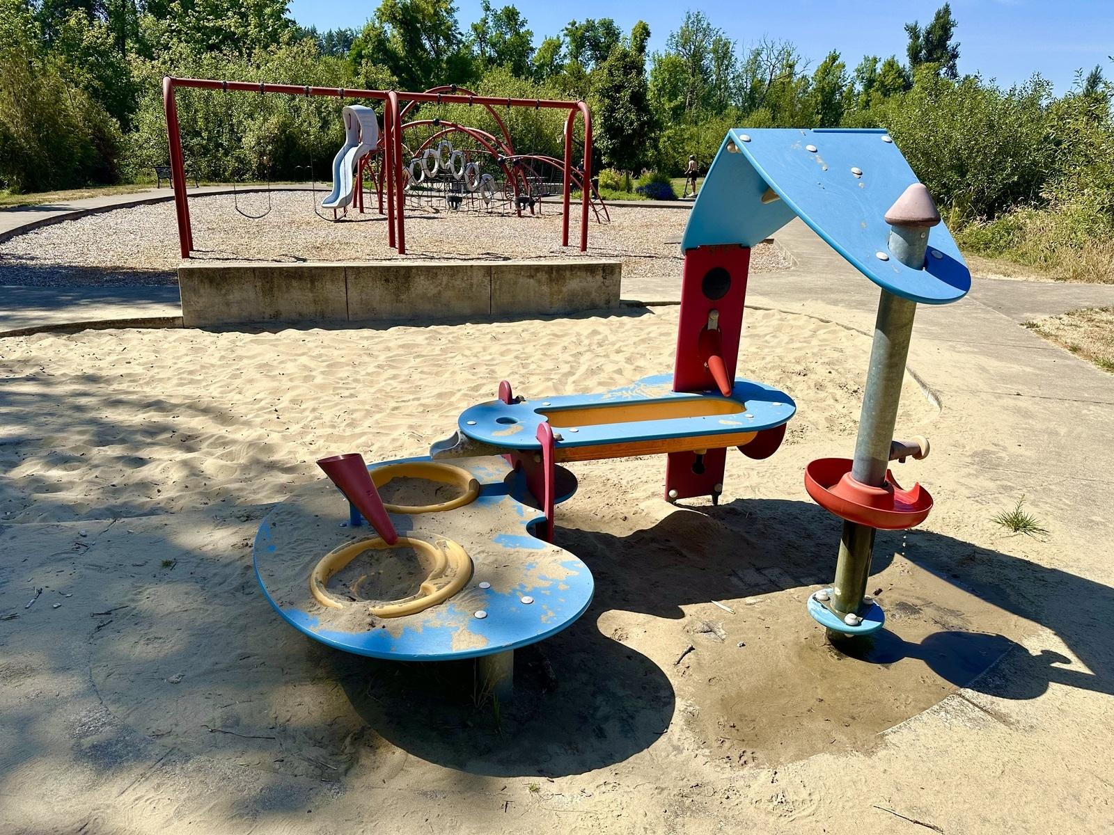 A sand and water play sits on one end of the playground at Jasper Meadows Park