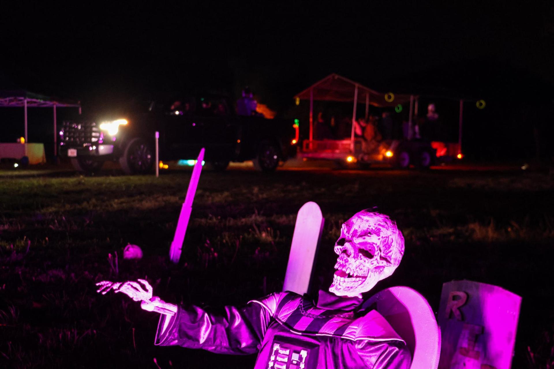a skeleton decoration lit up with pink lights with a hayride trailer behind it