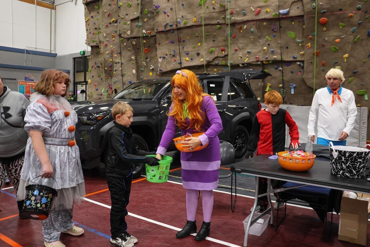 A child takes candy from someone dressed in costume in front of a truck and climbing wall.
