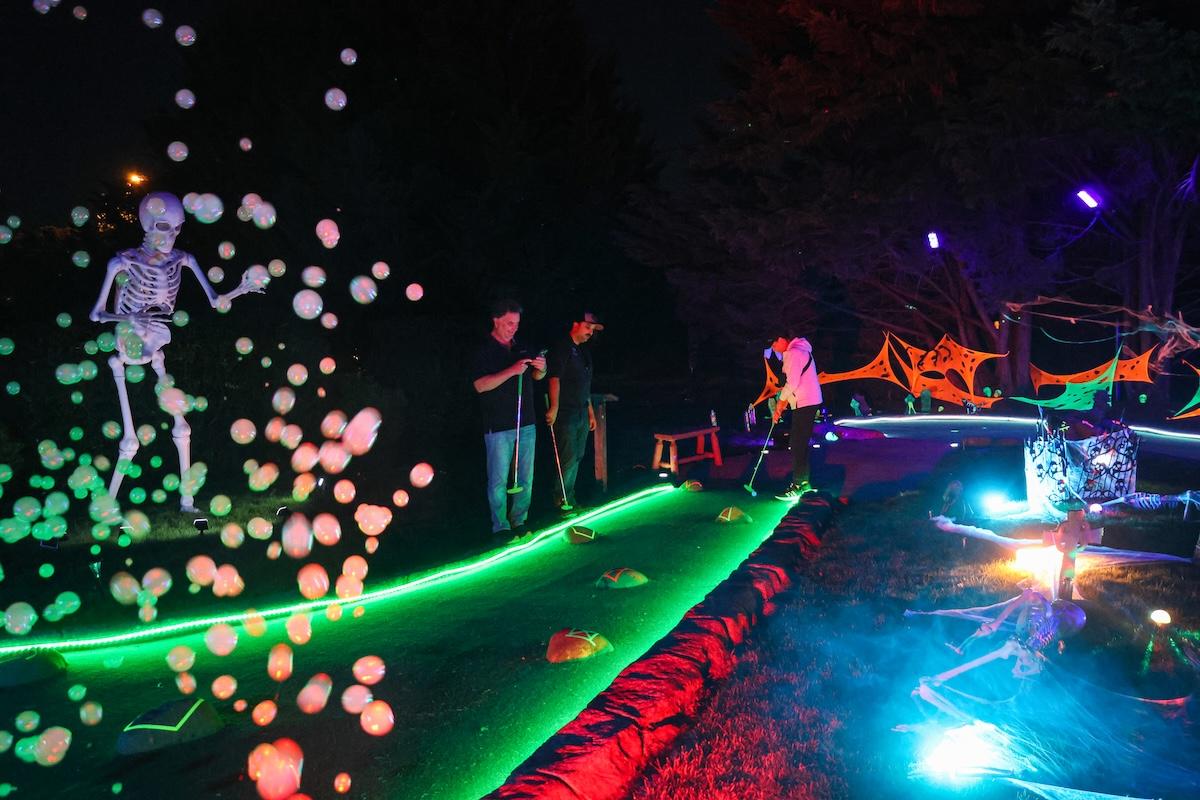 A mini golf course at night with colorful lights and fog bubbles floating in the air.