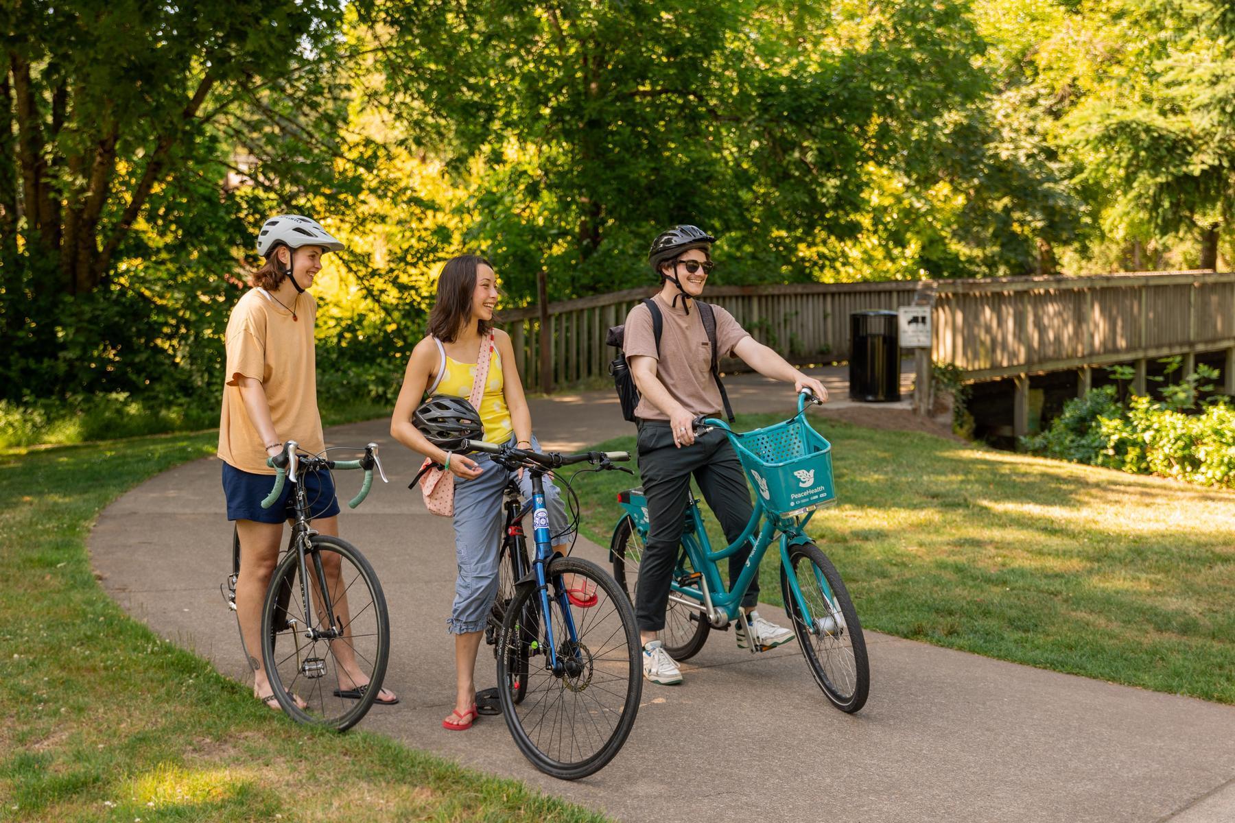 Three people ride bikes on a paved path through Island Park