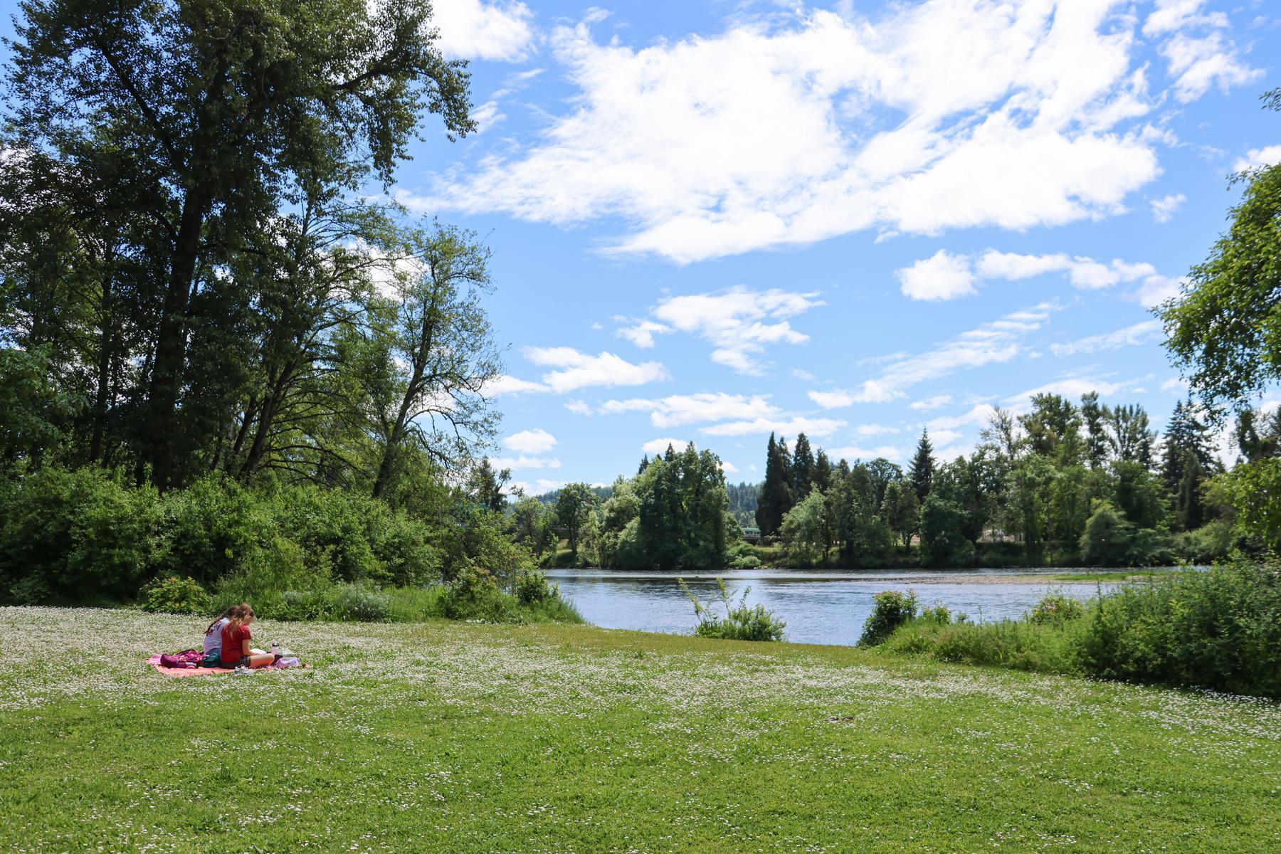 Two people sit on a picnic blanket and view the river from Island Park