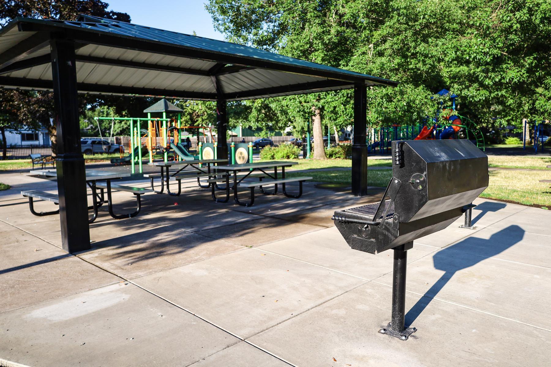 An outdoor BBQ sits next to covered picnic shelters at Meadow Park