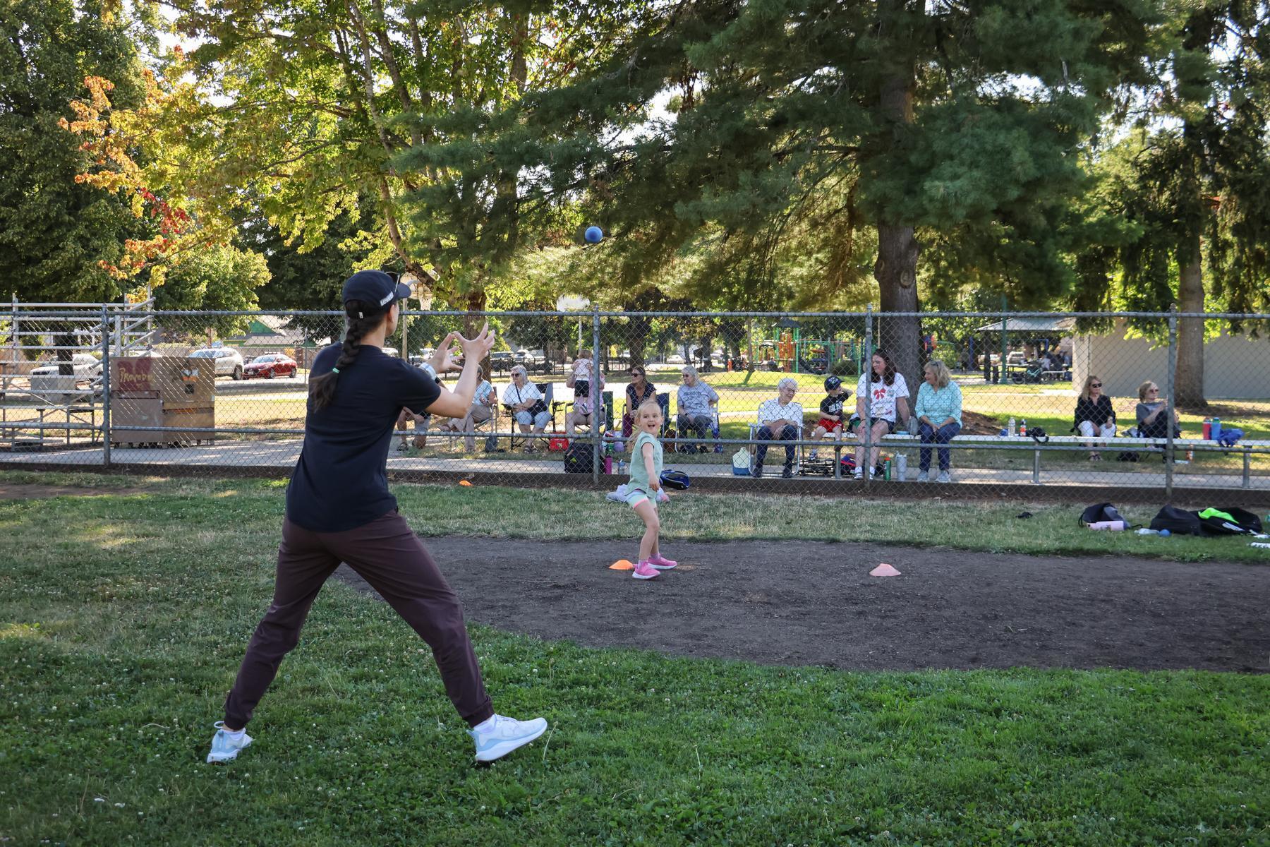 An adult and child play catch in the outdoor ball park at Meadow Park