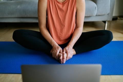 Woman stretching on a yoga mat infront of her computer